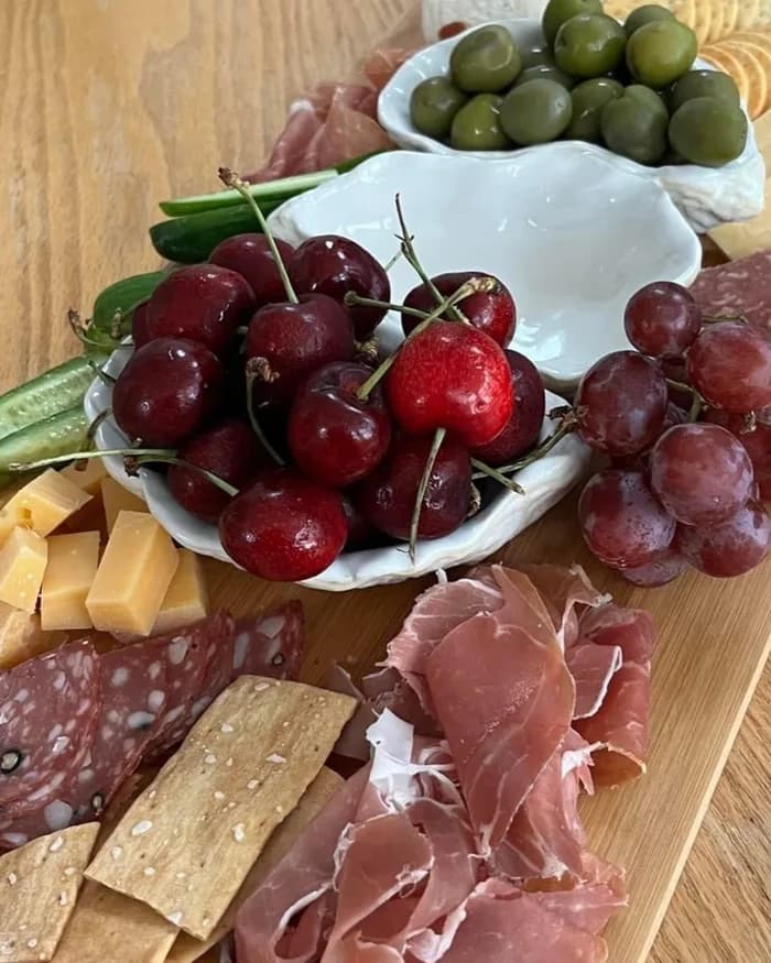 A cheese board with sliced cheeses, cured meat, grapes and crackers